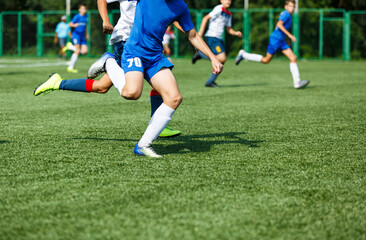 Obraz premium Young sport boys in blue sportswear running and kicking a ball on pitch. Soccer youth team plays football in summer. Activities for kids, training 