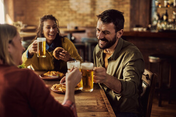 Happy man and his friends toasting with beer while eating in a pub.