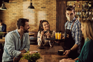 Waiter with protective face mask serving coffee to customers in a pub.