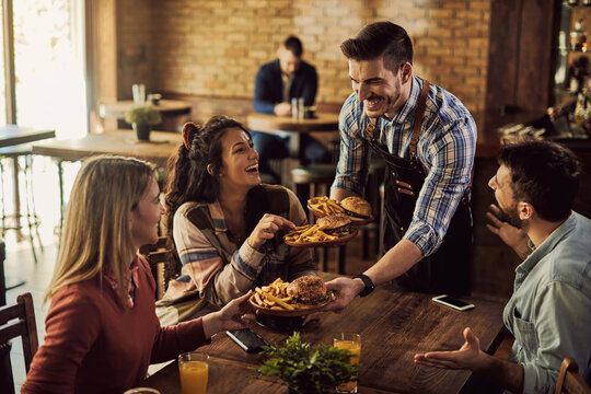 Happy waiter serving food to group of friends in a pub. - Powered by Adobe