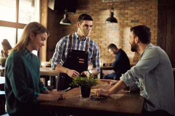Happy waiter wearing face mask while talking to customers n a pub.