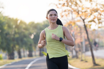 A young Asian woman runner athlete in sports outfit jogging and workout in the city park in the morning. Healthy lifestyle young sporty asian woman running at tropical park. Sport and recreation