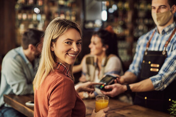 Happy woman paying bill in a pub and looking at camera.