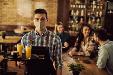 Portrait of waiter wearing face mask while working in a cafe during coronavirus pandemic.