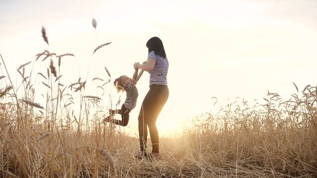 mom play with her daughter the park in wheat field. happy family people in the park concept. mom play is spinning daughter holding hands in wheat field. childhood dream fun happy family