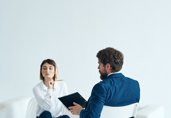 A woman psychologist with documents sits on the couch and a man on a chair in a suit