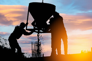 Silhouettes of construction workers pouring concrete mix at the building site background sunset sky