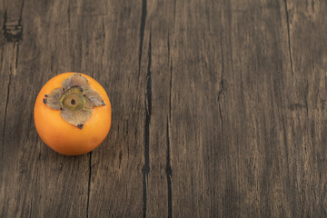One ripe persimmon fruit placed on wooden surface