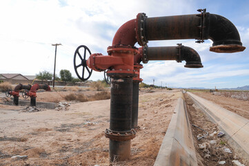 Irrigation pipe valve system beside concrete-lined canal in agricultural area, used to regulate water flow for crop fields in arid farmland infrastructure