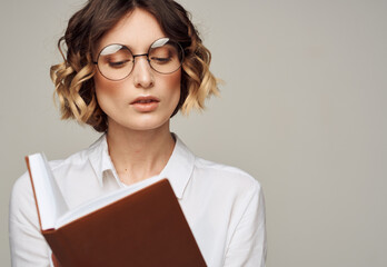 Smart woman with a notebook in her hands and in a white shirt on a gray background cropped view