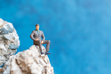 Miniature people Businessman sitting on the rock with blue background
