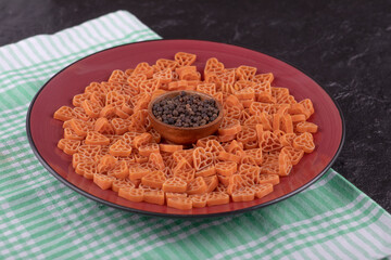 A plate of raw pasta in hearts shape with pepper on black table