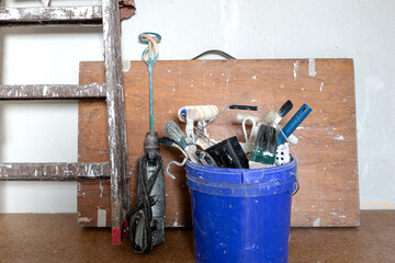 Painter equipment. Ladder and wooden table on the wall. Paint brushes and paint roller in the bucket