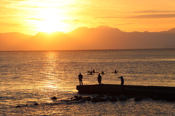 Naklejka na ściany i meble 片瀬江ノ島海岸から見る伊豆半島に沈むオレンジ色の夕日と堤防のシルエット