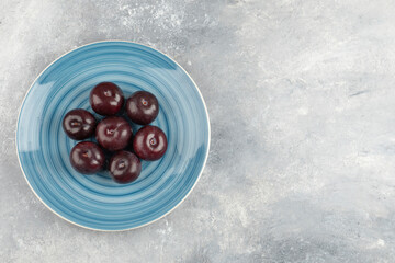 Blue plate of fresh purple plums on marble surface