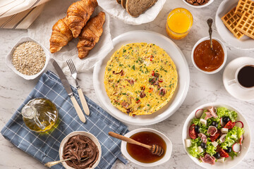 Broad assortment of food including omelette, croissants, salad, bread, oatmeal, jam, waffles, honey, choclate spread, coffee and orange juice served on a table