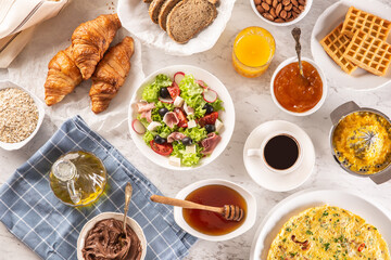 Broad assortment of food including omelette, croissants, salad, bread, oatmeal, jam, waffles, honey, choclate spread, coffee and orange juice served on a table