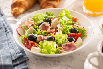 Healthy salad in a bowl with olives, raddishes, tomato, cheese and lean ham served for breakfast