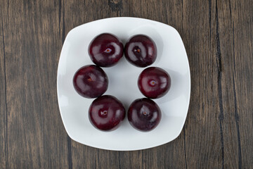 A white plate of fresh delicious plums on wooden table