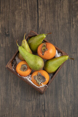 Delicious fuyu persimmons and ripe pears in wooden box