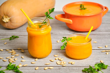 Pumpkin smoothies on a rustic gray background and decoration we have the pipes and pumpkin, also a pumpkin puree in a small orange pot. Gray and orange predominate to highlight the pumpkin