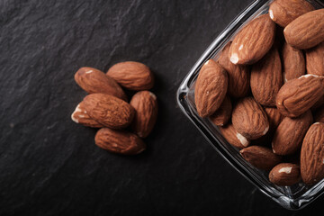 Almonds in a small glass plate, top view, on a dark background, close up