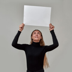 Happy young caucasian woman with long hair dressed in black turtleneck looking up while holding...