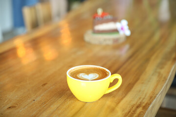 Coffee with a heart-shaped face Put in a yellow cup Placed on a wooden table