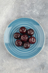 Blue plate of fresh purple plums on marble surface