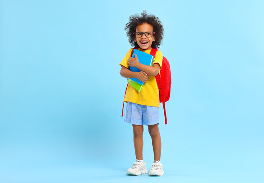 Cheerful little ethnic schoolchild with backpack and textbooks in studio