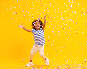 Excited African American kid jumping and catching confetti in studio - obrazy, fototapety, plakaty