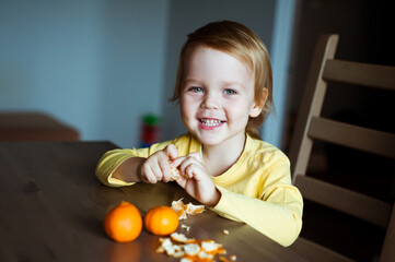 Cute bright boy cleans and eats tangerines. Healthy food.