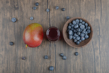 Whole mango, blueberries and fresh glass of juice on wooden table