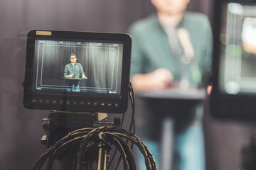 Young journalist in a television recording studio is talking into a microphone, blurry film cameras