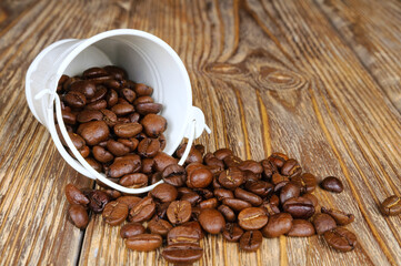 Small white metal bucket with roasted coffee beans on wooden background. Close-up