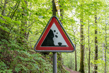 Red warning sign for falling rocks in forest steep incline.