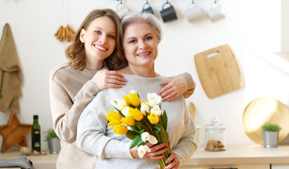 Obraz na płótnie Canvas Delighted young woman hugging mother with bouquet of fresh tulips