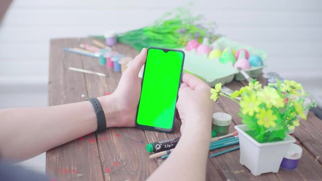 A man prepares for Easter, paints Easter eggs and uses a smartphone with chroma key