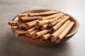 Aromatic cinnamon sticks in bowl on grey stone table, closeup