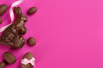 Flat lay composition with chocolate Easter bunny and eggs on pink background. Space for text