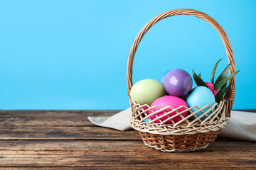 Colorful Easter eggs in wicker basket on wooden table. Space for text