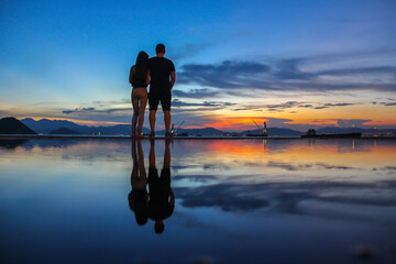 silhouette and reflection of romantic boy and girl friends holding hands and enjoying sunset at...
