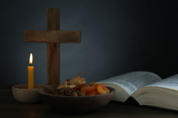 Cross, Bible, candle and dried fruits on wooden table, space for text. Lent season
