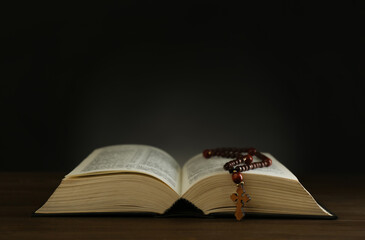 Open Bible and rosary beads on wooden table, space for text. Lent season