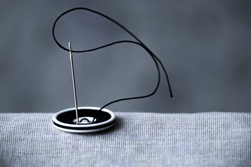 The black and white button is sewn with a sewing needle and black thread to hold the two fabrics together in close-up. Photo for an article about sewing hobbies and sewing.
