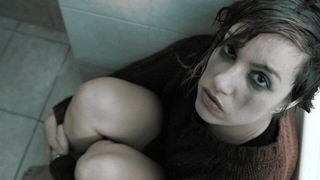 suffering, depression - girl squatting in the bathroom stares at camera 
