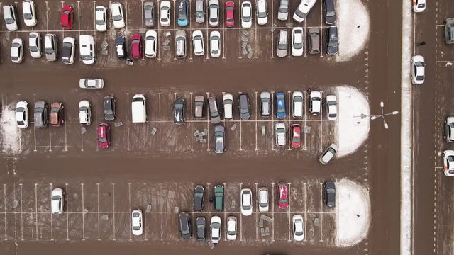 Passenger cars are parked in straight rows in a wide parking lot. Bird's-eye view of a large number of cars. Vehicles are standing near the mall, and the owners have gone off to shop at a discount.