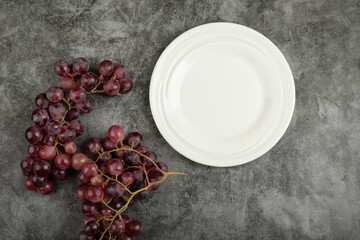 Fototapeta na wymiar White plate and red delicious grapes on marble table
