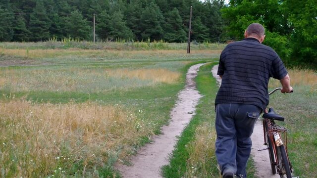 Senior man walking (admittedly thief) with very old rust bicycle on country road and being dissatisfaction about quality of the bike
