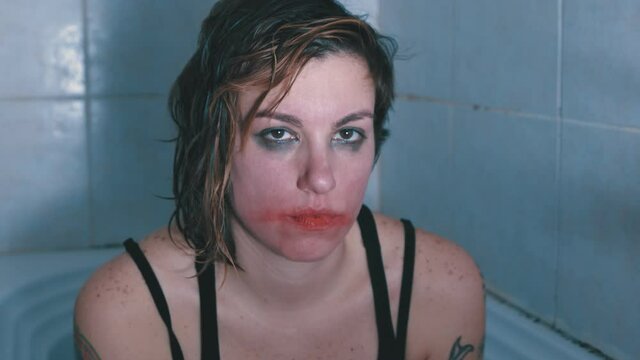madness, alienation - girl in the bathtub with loose lipstick on her face laughs